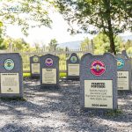 Several Ben & Jerry's flavor grave markers in a sunny, fenced yard, each with colorful logos and inscriptions.