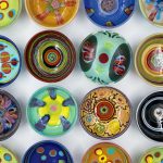 A collection of sixteen colorful, hand-painted ceramic bowls with various abstract patterns, arranged in a grid on a white background.
