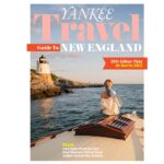 A woman sits on a boat facing a coastal lighthouse at sunset, featured on the cover of Yankee Travel Guide to New England.