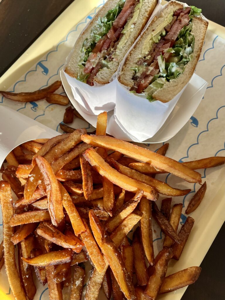 At Paco Submarine in New Smyrna Beach, Florida, a sandwich cut in half with lettuce, tomato, bacon, and mayo sits next to a pile of French fries on a yellow tray.