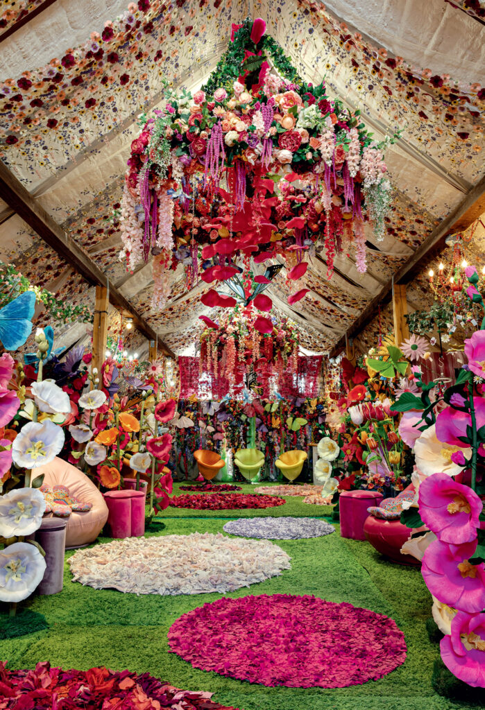 Best Things to Do in Vermont This Summer. A long, flower-filled room with flower petal rugs, artificial grass, colorful large flowers, and hanging floral arrangements under a decorated ceiling.