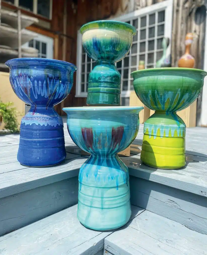 Four colorful ceramic vases with unique, round shapes and vibrant patterns are displayed on blue wooden steps outdoors.