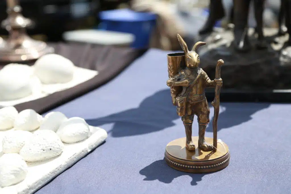 A small bronze rabbit figurine stands on a table holding a staff and horn, surrounded by other decorative items.