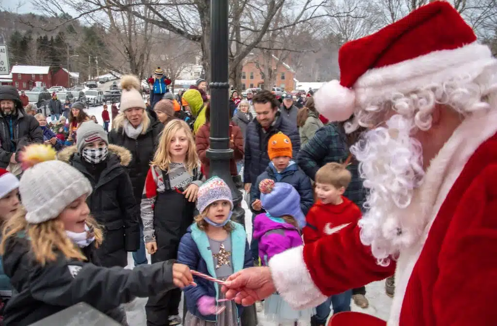 Santa handing out candy canes to a group of children outdoors during a festive event.